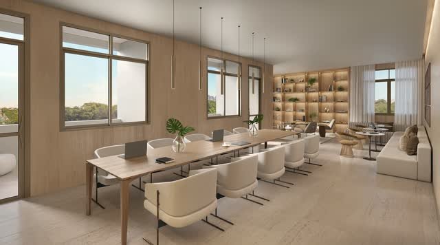 Coworking com mesa longa de trabalho, cadeiras, estantes iluminadas e área de lounge